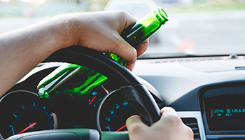 A driver holding a beer bottle in one hand